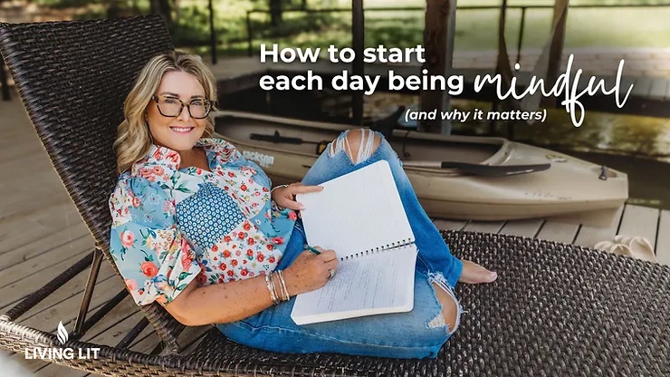 Woman in floral blouse and jeans writing in a notebook on a wicker chair. Text: "How to start each day being mindful." Calm outdoor setting.