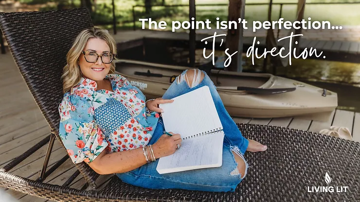 Michelle in a floral shirt sits on a wicker chair, writing in a notebook. Background shows a kayak. Text: "The point isn’t perfection... it’s direction."